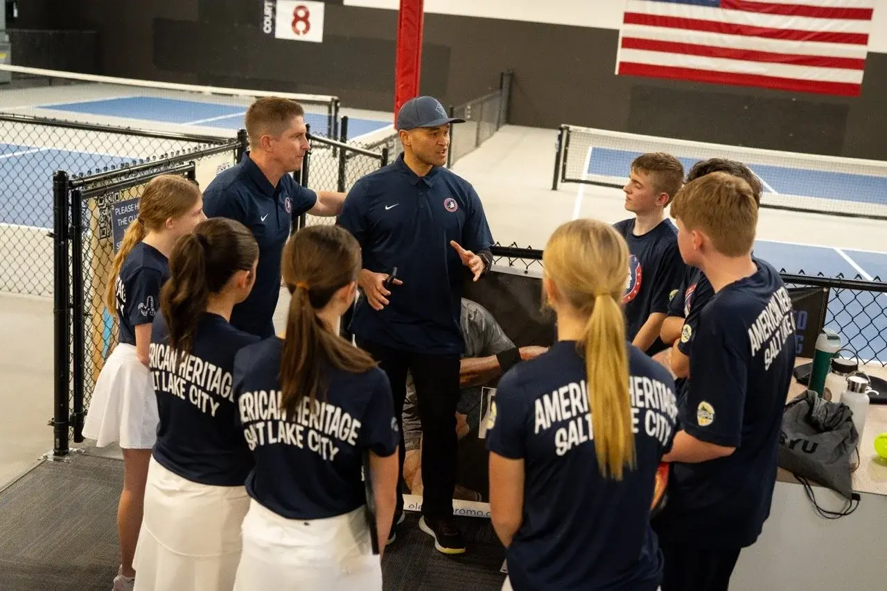 High school pickleball team and coaches in a huddle beside indoor courts